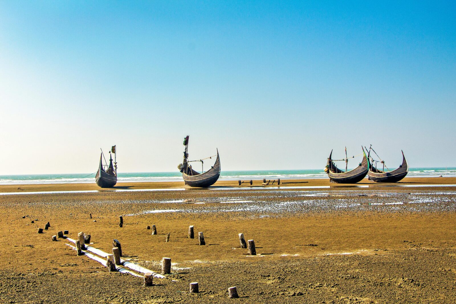 Traditional wooden boats on the sandy shores of Cox's Bazar, Bangladesh under a clear blue sky.